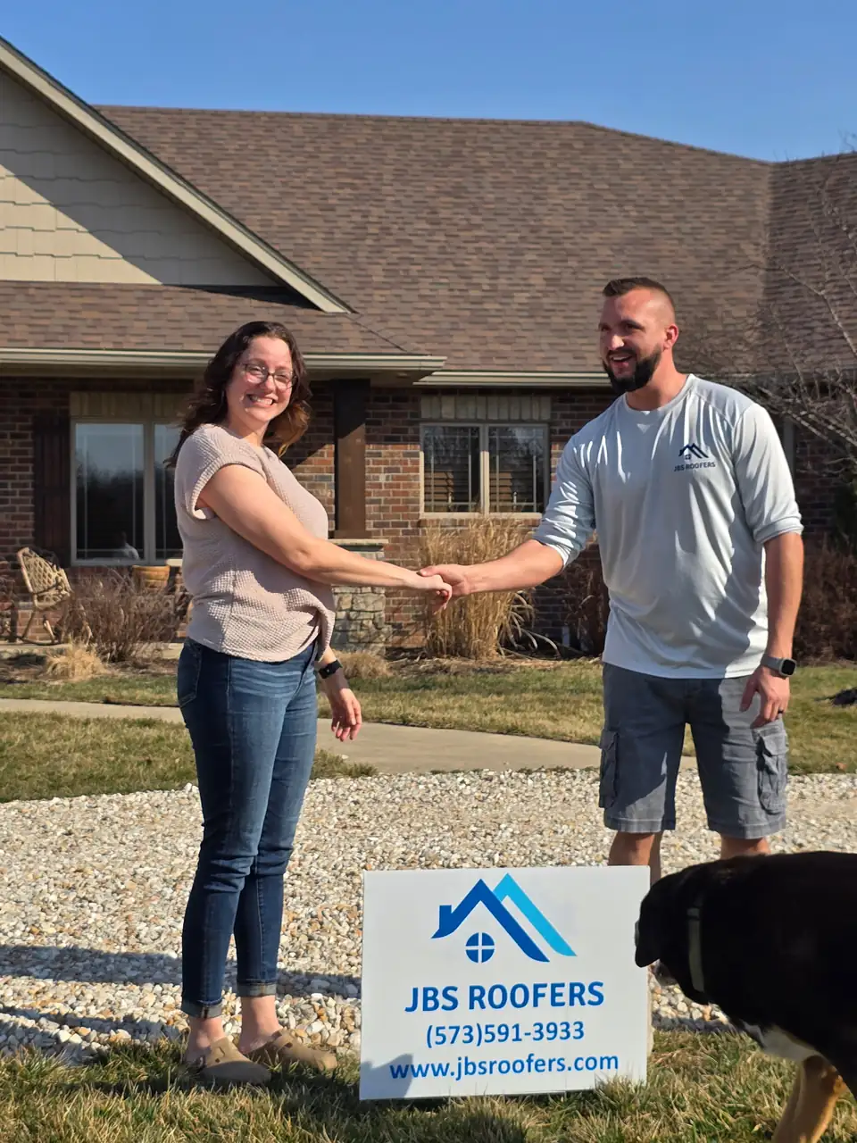 Homeowner shaking hands with a JBS Roofers team member next to a JBS Roofers yard sign
